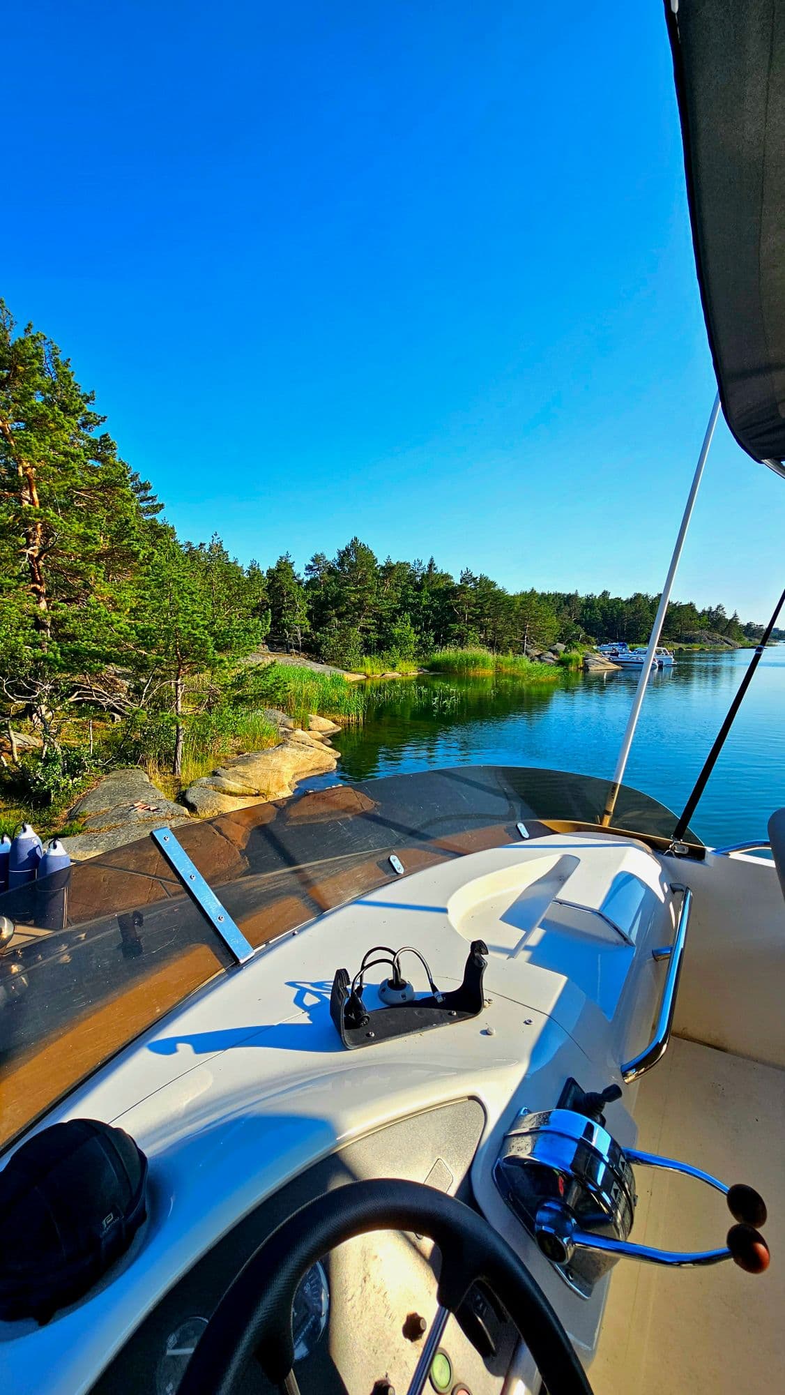 Utsikt från båtens förarplats över en lugn vik i skärgården en solig dag